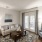 Spacious and well lit living room with wood floors and a large window with access to the kitchen