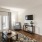 Spacious and well lit living room with wood floors and a large window with access to the kitchen